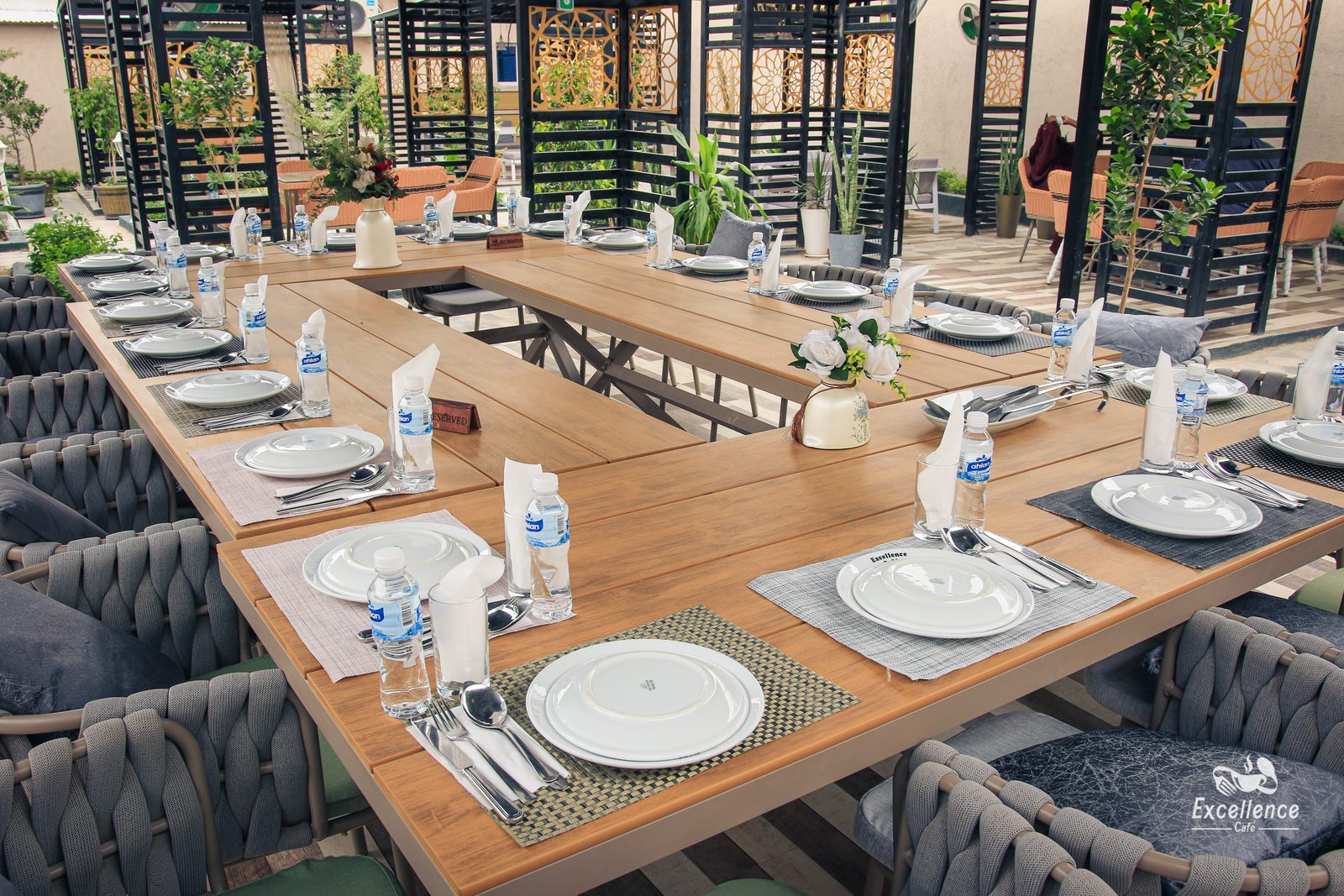 A long U-shaped table on Excellence Café's terrace, laid with branded plates and a "reserved" marker for a private group.