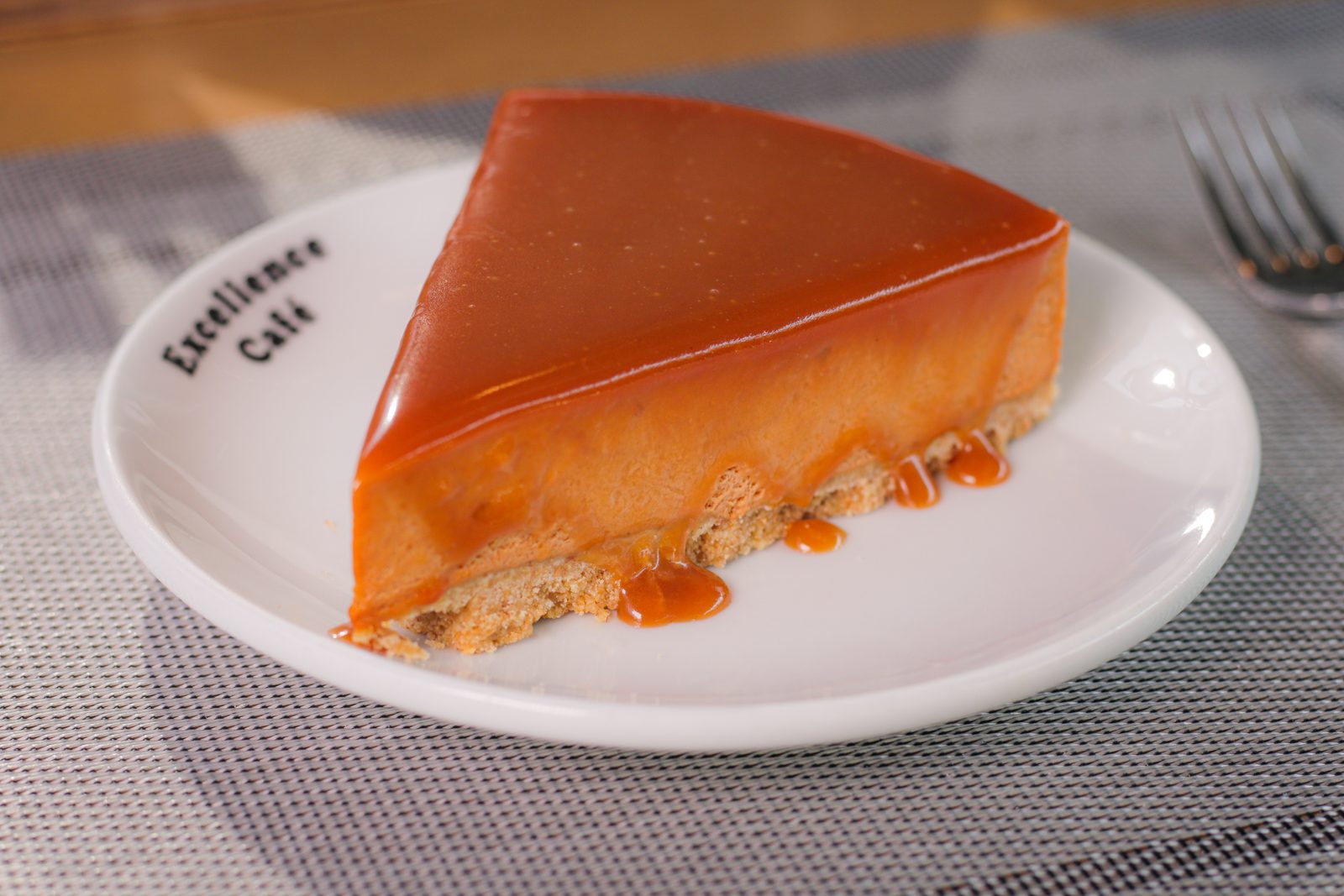 A slice of caramel cheesecake on an Excellence Café branded plate.