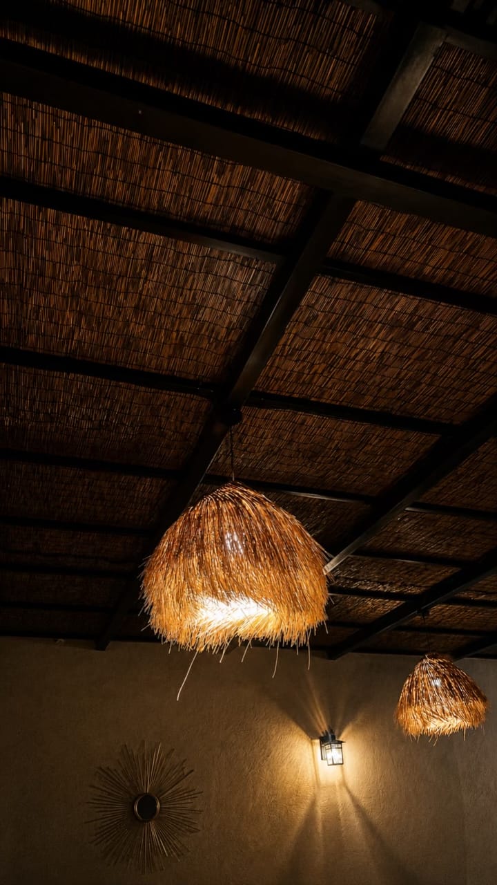 The Village Hargeisa ceiling — a timber-beamed reed ceiling with a large woven straw pendant lamp glowing warm.